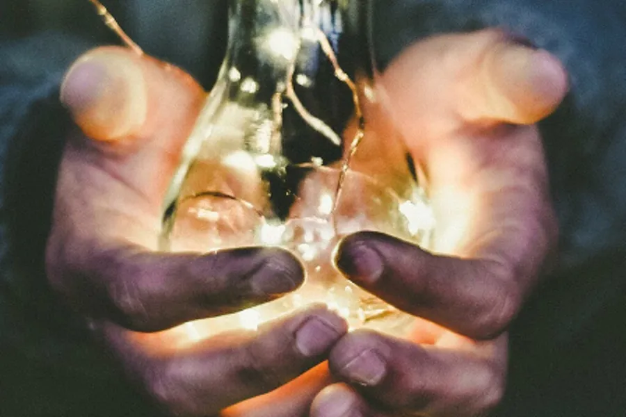 Hendler som holder en lyspære som lyser.