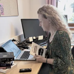 En forsker som ser på en bærbar datamaskin med håndbok i sykepleie i hendene