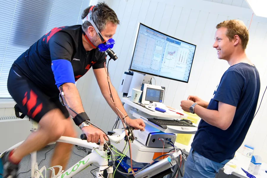 Mann på sykkel med pustemaske og forsker ved målestasjon.